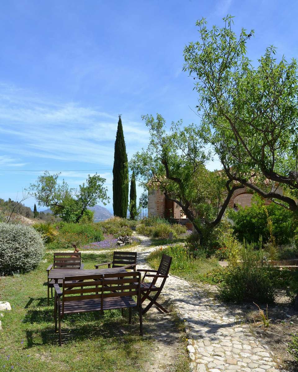 Jardín de una casa rural en la Vall de Laguar con mesas de madera, olivos y cipreses