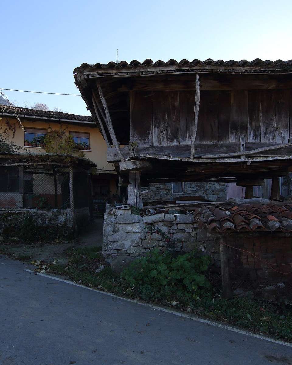 Hórreo de madera junto a una carretera de aldea en Laviana, con casas detrás
