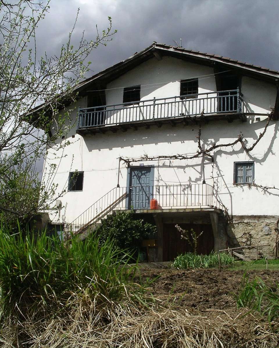 Caserío blanco de dos plantas con balcón de madera y huerta delante