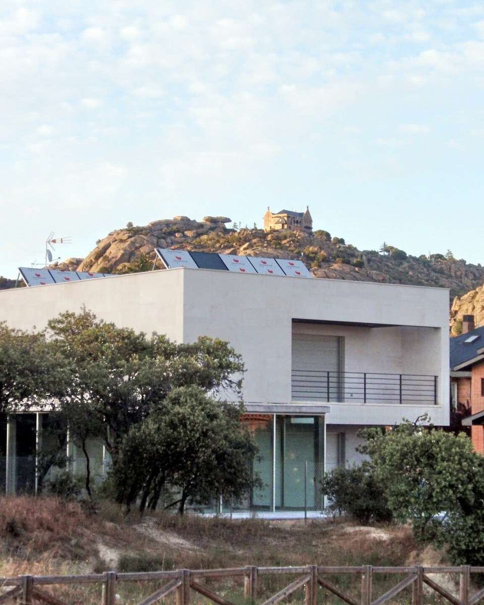 Chalé blanco de dos plantas entre encinas en una urbanización de Torrelodones, con rocas de granito detrás