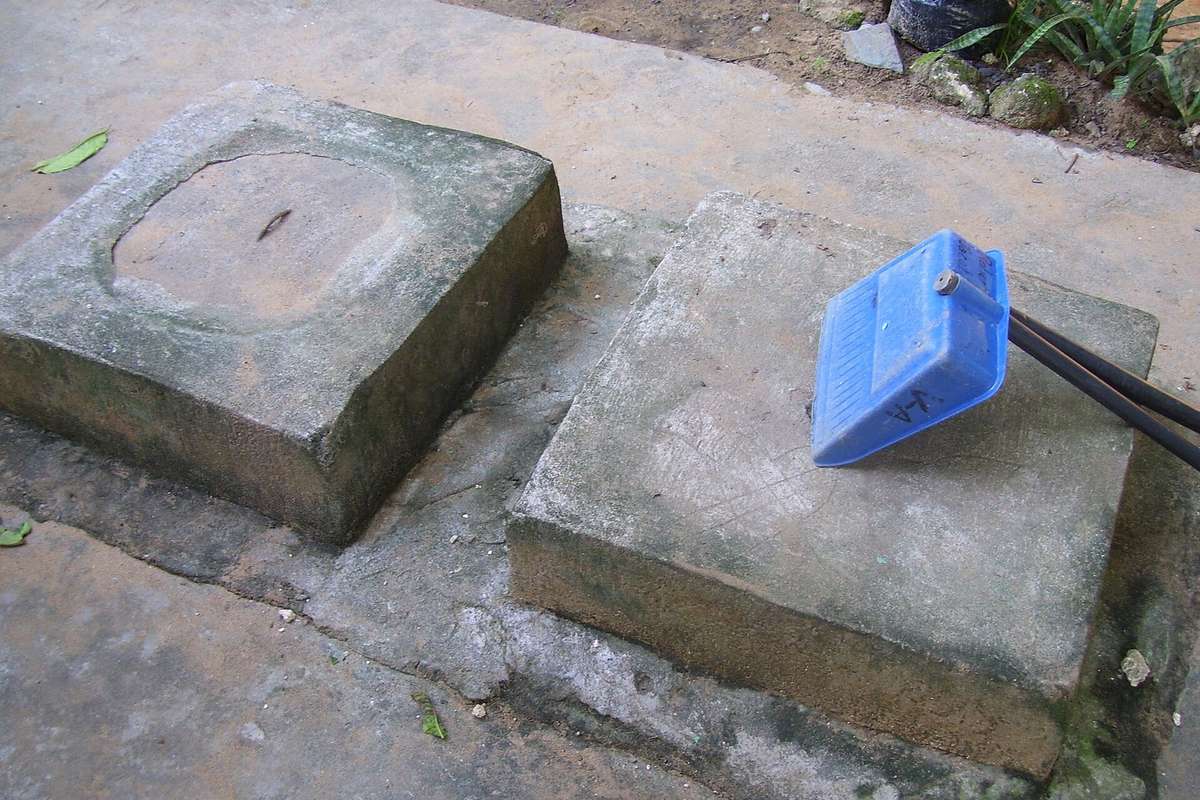 Dos tapas de registro de hormigón de una fosa séptica, con un cepillo de plástico apoyado