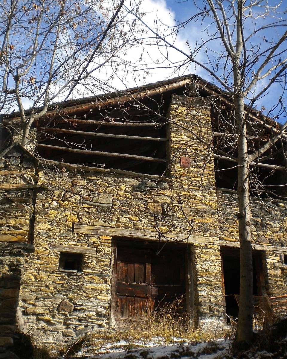 Construcción antigua de piedra con puertas de madera, entre árboles sin hojas